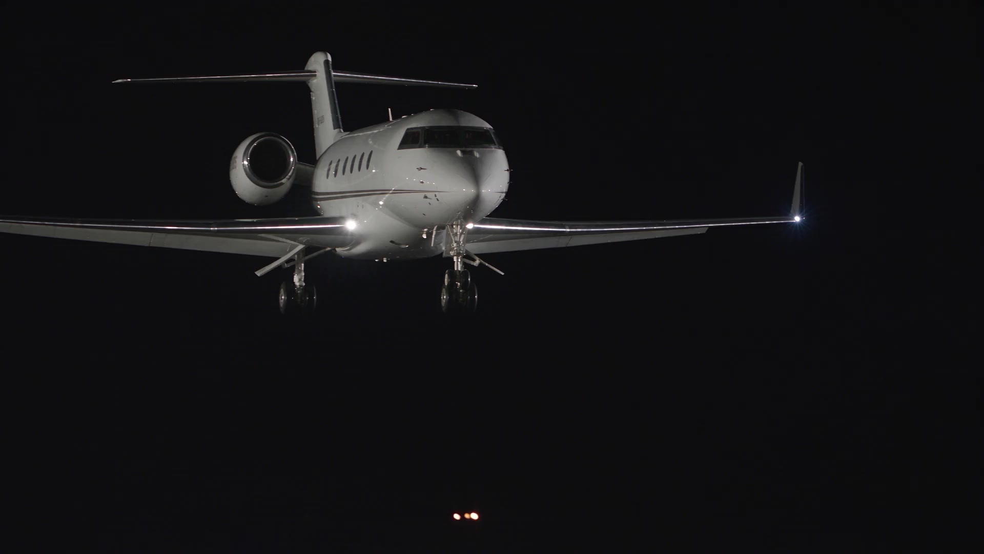 A polished white private jet approaching a runway at night